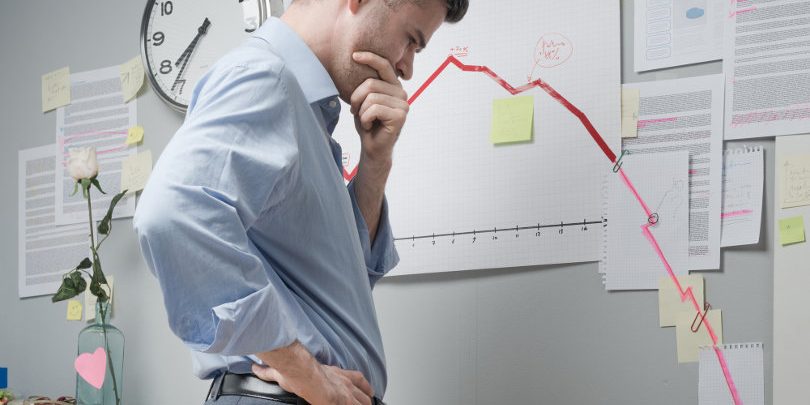 Concerned businessman at work looking at negative business chart with arrow going downwards.